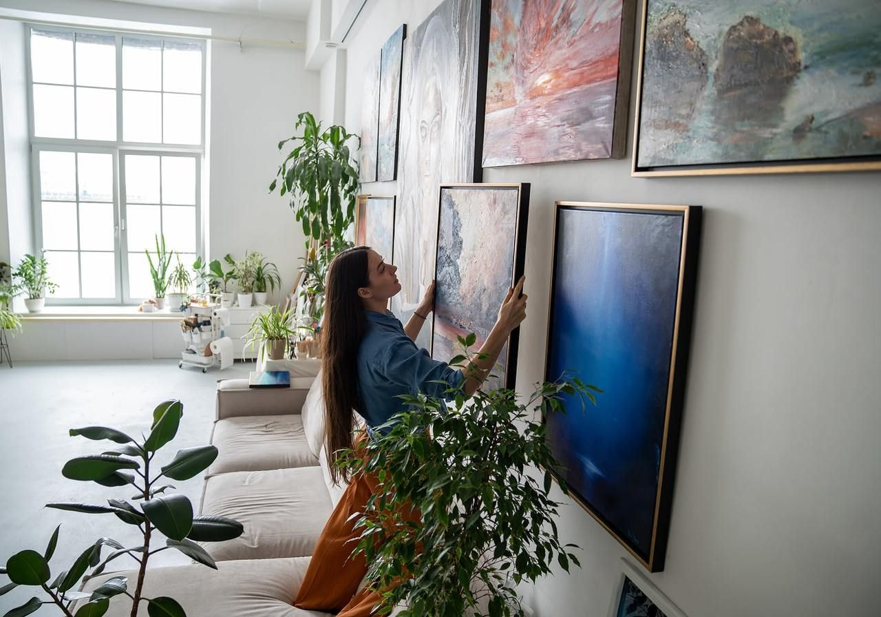 A woman gazes thoughtfully at various pieces of art displayed on a gallery wall.